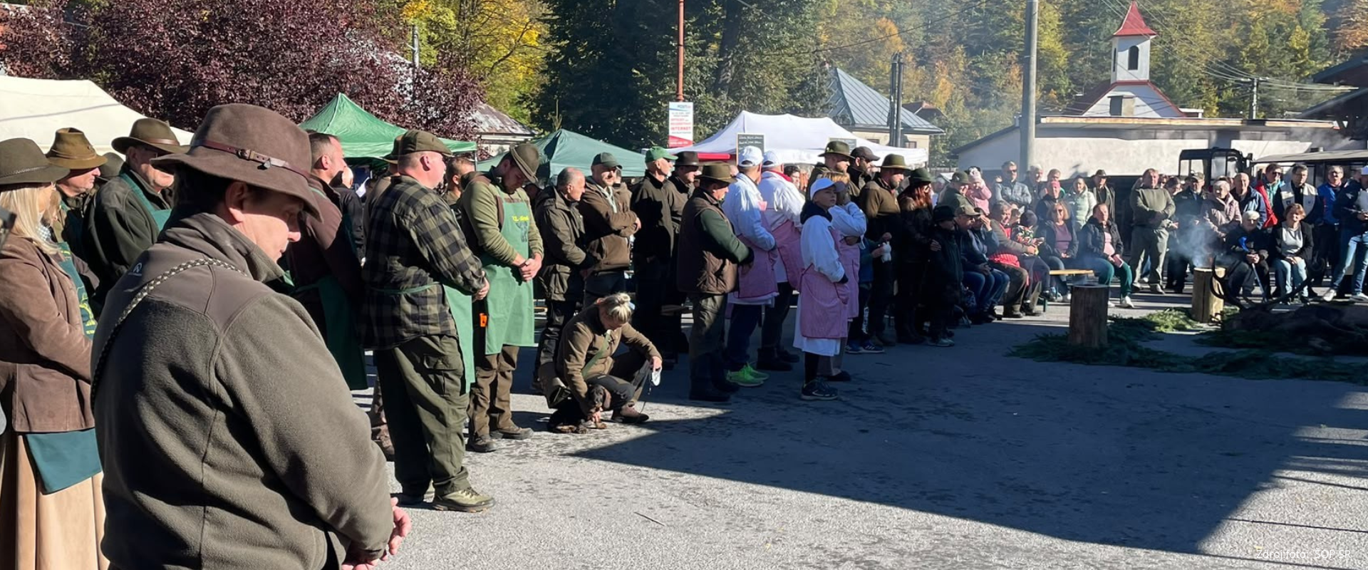 Účastníci poľovníckeho podujatia v Ponickej Hute počas spoločného programu, v pozadí stánky a jesenná krajina.